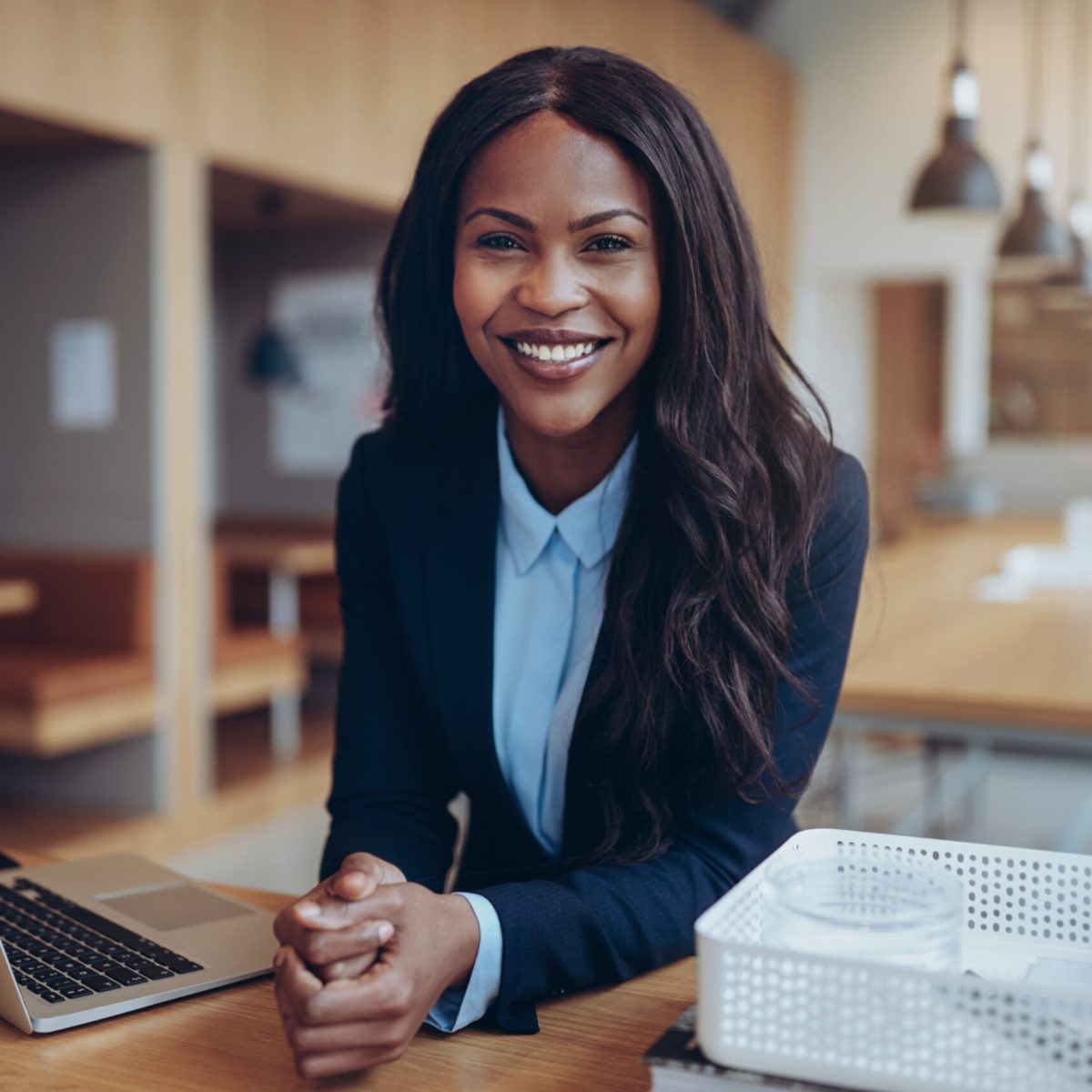 Smiling young African American businesswoman leaning on a table in an office lounge working on a laptop